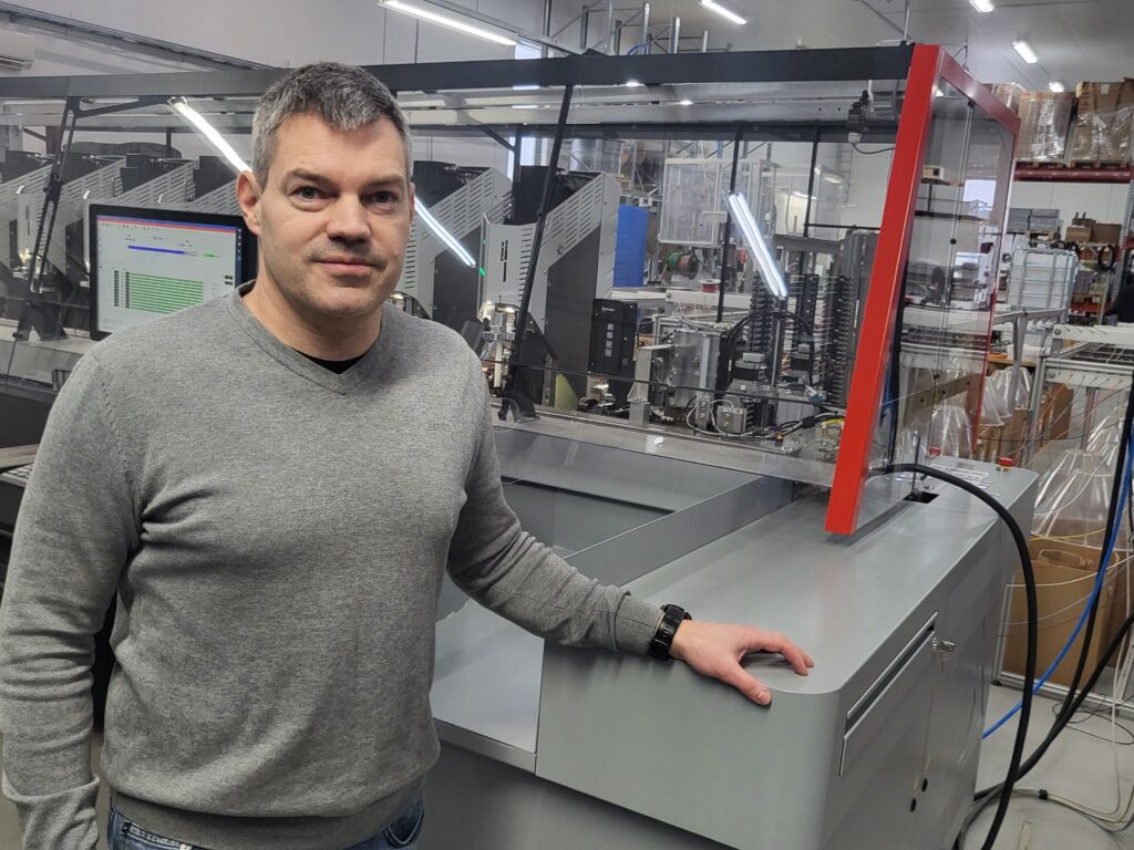 Tomas Grynngärds takanaan johdinsarjavalmistukseen käytetty automaattikone. Tomas Grynngärds framför en automatmaskin för kablagetillverkning. 